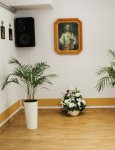 Wnętrze Domu Pomocy Społecznej. Brązowa drewniana podłoga. Kremowe ściany. Na podłodze kwiaty doniczkowe. Na ścianach obrazy religijne